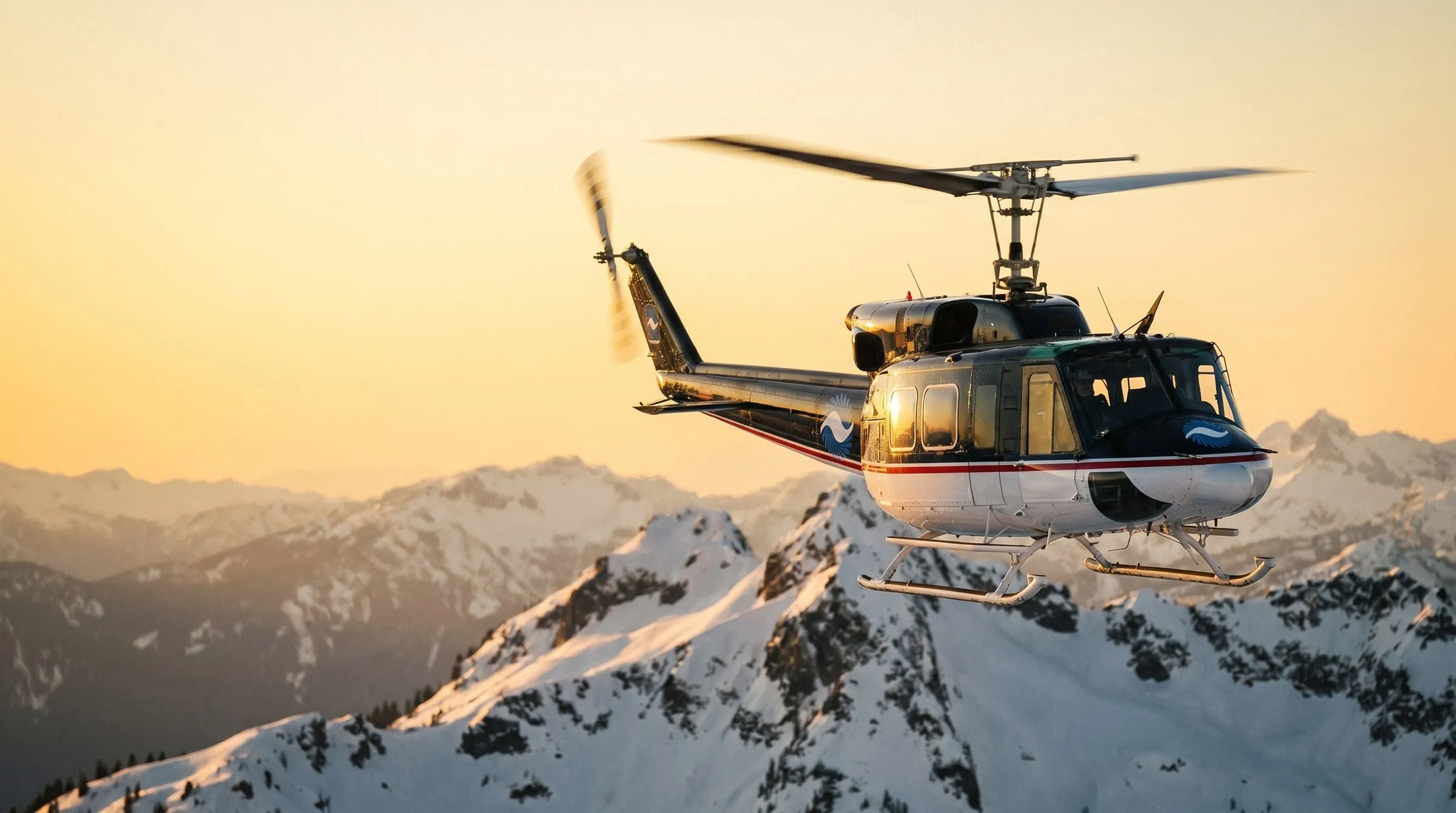 A Coldstream Bell 212 helicopter cruising over snow-covered mountains at golden hour