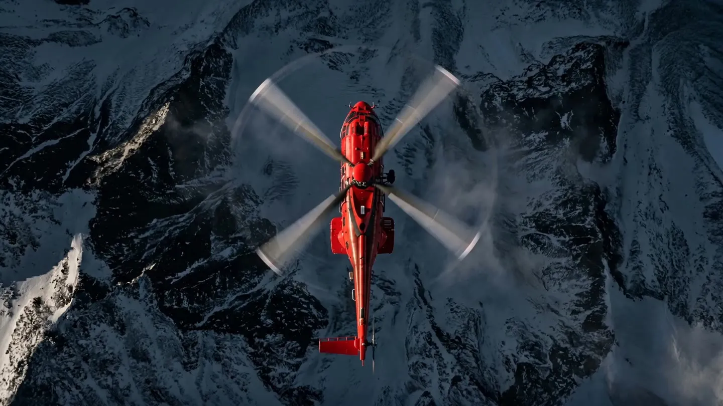 Aerial top-down view of a red Coldstream Super Puma helicopter in flight over snow-covered mountain peaks